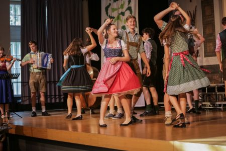 Tanzgruppe in Tracht auf der Bühne, links begleitet ein Akkordeonspieler