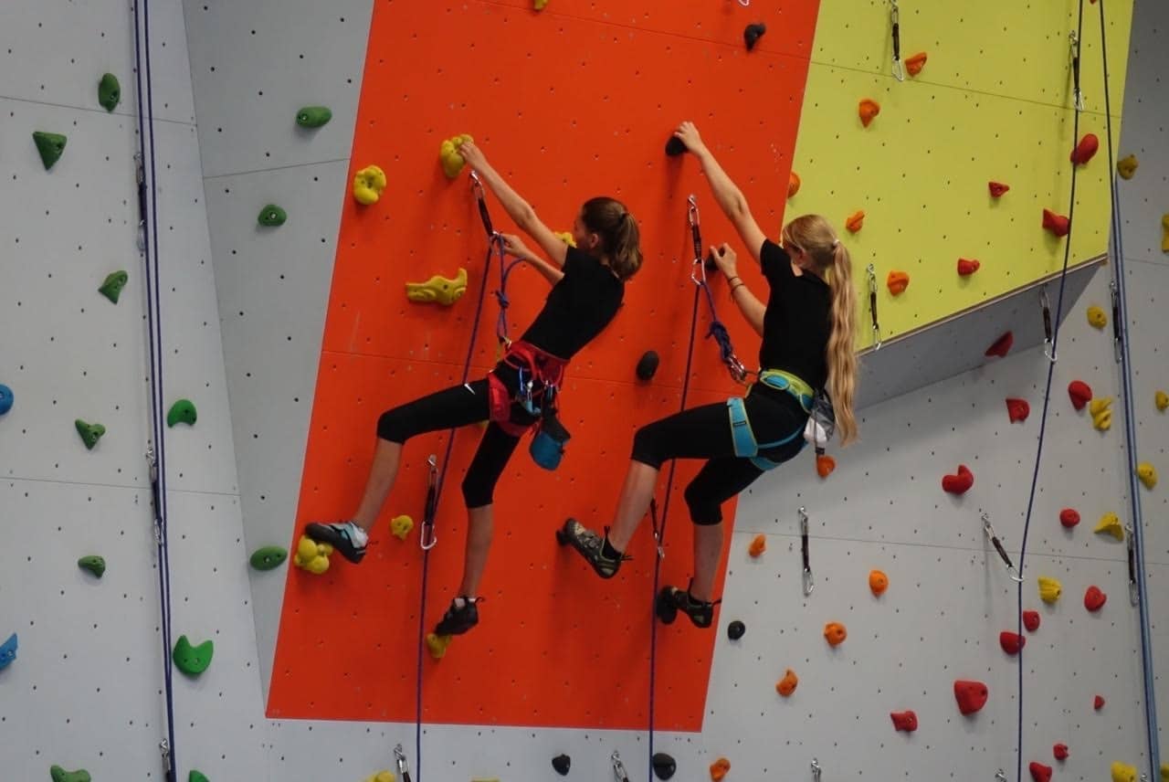 Zwei Schülerinnen klettern gesichert die farbige Kletterwand hinauf