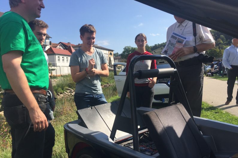 Schüler erklären Besuchern das offene Elektrofahrzeug im Freien
