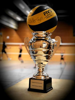 Der Siegerpokal mit aufgesetztem Volleyball in der Sporthalle
